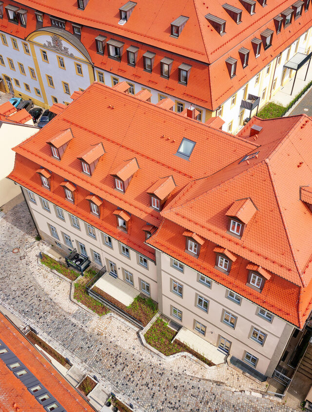 Drone aerial photograph of renovated Carmelite Monastery building with red tile roof, dormer windows and cobblestone courtyard in historic Bamberg