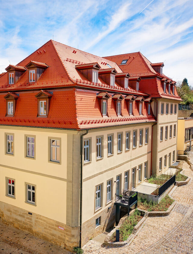 Wide aerial view of renovated Carmelite Monastery Bamberg with red tile roofs, cream-colored facades, dormer windows and cobblestone courtyard in landmark ensemble