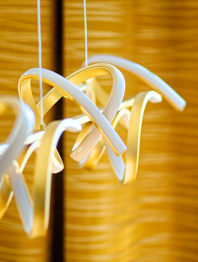 Close-up of modern sculptural pendant light with twisted gold and white metal rings over dining area in premium furnished apartment Bamberg