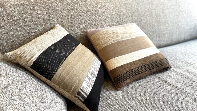Close-up of designer sofa with decorative cushions in striped and textured patterns, natural gray and beige tones with different weaving structures on salt-and-pepper upholstery in furnished apartment Bamberg