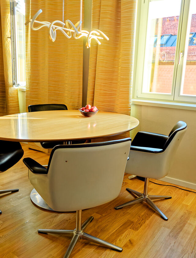 Bright dining room with Pierre Paulin designer table, Friso Kramer swivel chairs, golden curtains and views of red tile roofs in furnished premium apartment Bamberg Carmelite Monastery