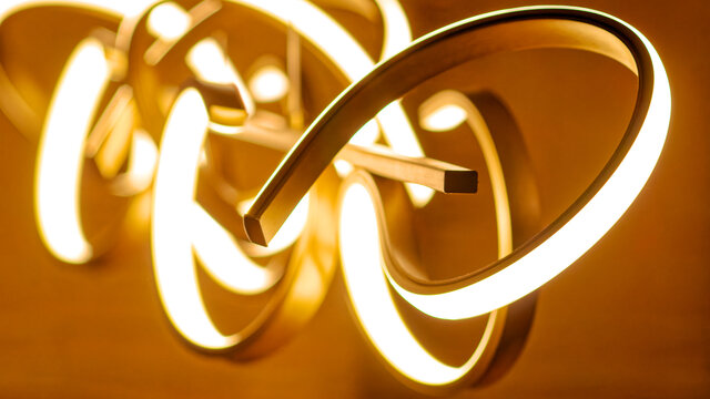 Close-up detail of illuminated sculptural pendant light with flowing gold and white metal rings creating warm ambient lighting in furnished apartment Bamberg
