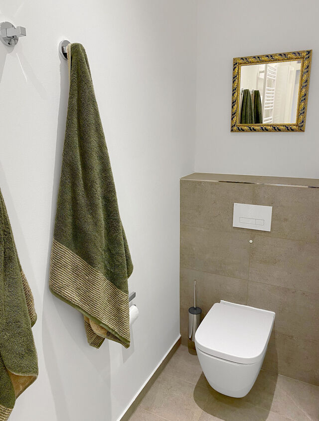 Modern wall-hung toilet with premium olive-green towels and ornate gold mirror in furnished apartment Bamberg
