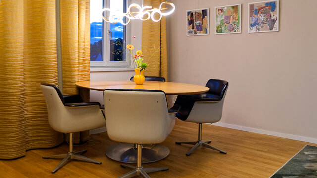 Bright dining room with Pierre Paulin designer table, Friso Kramer swivel chairs, golden curtains and views of red tile roofs in furnished premium apartment Bamberg Carmelite Monastery
