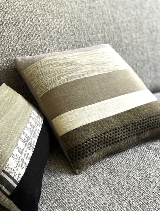 Close-up of designer sofa with decorative cushions in striped and textured patterns, natural gray and beige tones with different weaving structures on salt-and-pepper upholstery in furnished apartment Bamberg