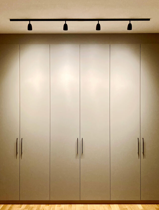 Large custom-made built-in wardrobe in light beige with metal handles, modern black track lighting and ornate mirror in bedroom hallway on oak parquet in furnished apartment Bamberg