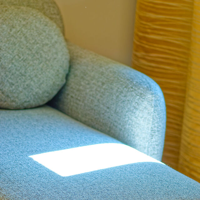 Close-up of designer sofa with high-quality salt-and-pepper gray melange upholstery fabric, warm sunlight spot and golden curtains in background in furnished apartment Bamberg
