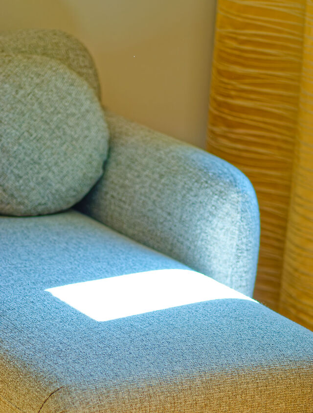Close-up of designer sofa with high-quality salt-and-pepper gray melange upholstery fabric, warm sunlight spot and golden curtains in background in furnished apartment Bamberg