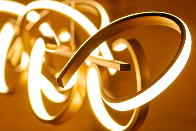 Close-up detail of illuminated sculptural pendant light with flowing gold and white metal rings creating warm ambient lighting in furnished apartment Bamberg