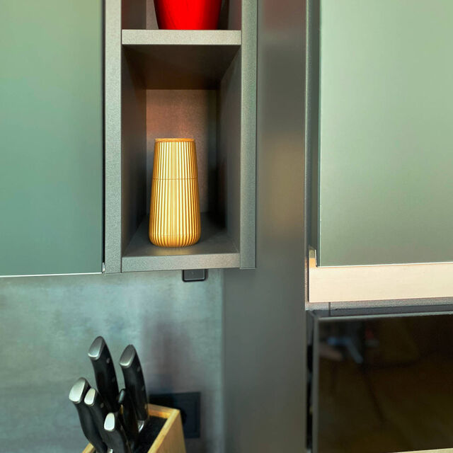 Close-up of mineral green ultra-matte Nobilia kitchen with open display niches, red designer vase, quality knife block and designer accessories on dark countertop in furnished apartment Bamberg