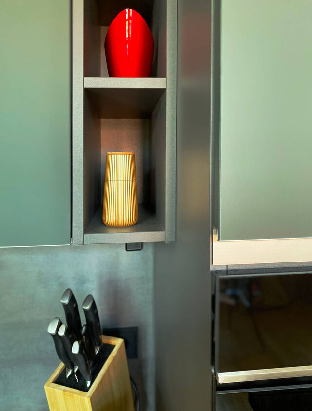 Close-up of mineral green ultra-matte Nobilia kitchen with open display niches, red designer vase, quality knife block and designer accessories on dark countertop in furnished apartment Bamberg