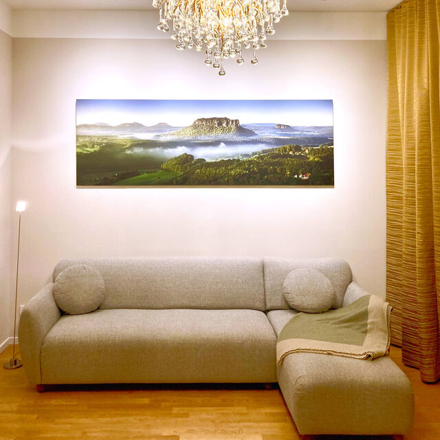 Evening view of living room with gray salt-and-pepper sofa, large-format landscape photograph Lilienstein III by Dirk Wiedlein, crystal Icicle chandelier by Paul Neuhaus and golden Zimmer & Rohde curtains in furnished apartment Bamberg