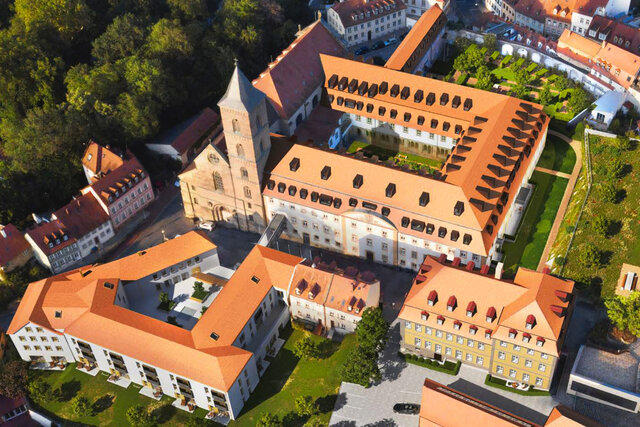 Drone aerial photograph of renovated Carmelite Monastery compound with church, red tile roof, dormer windows and cobblestone courtyard in historic Bamberg