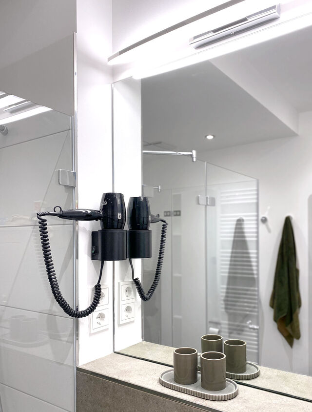 Modern bathroom mirror with LED lighting, wall-mounted hairdryer and elegant ceramic bathroom accessories in furnished apartment Bamberg